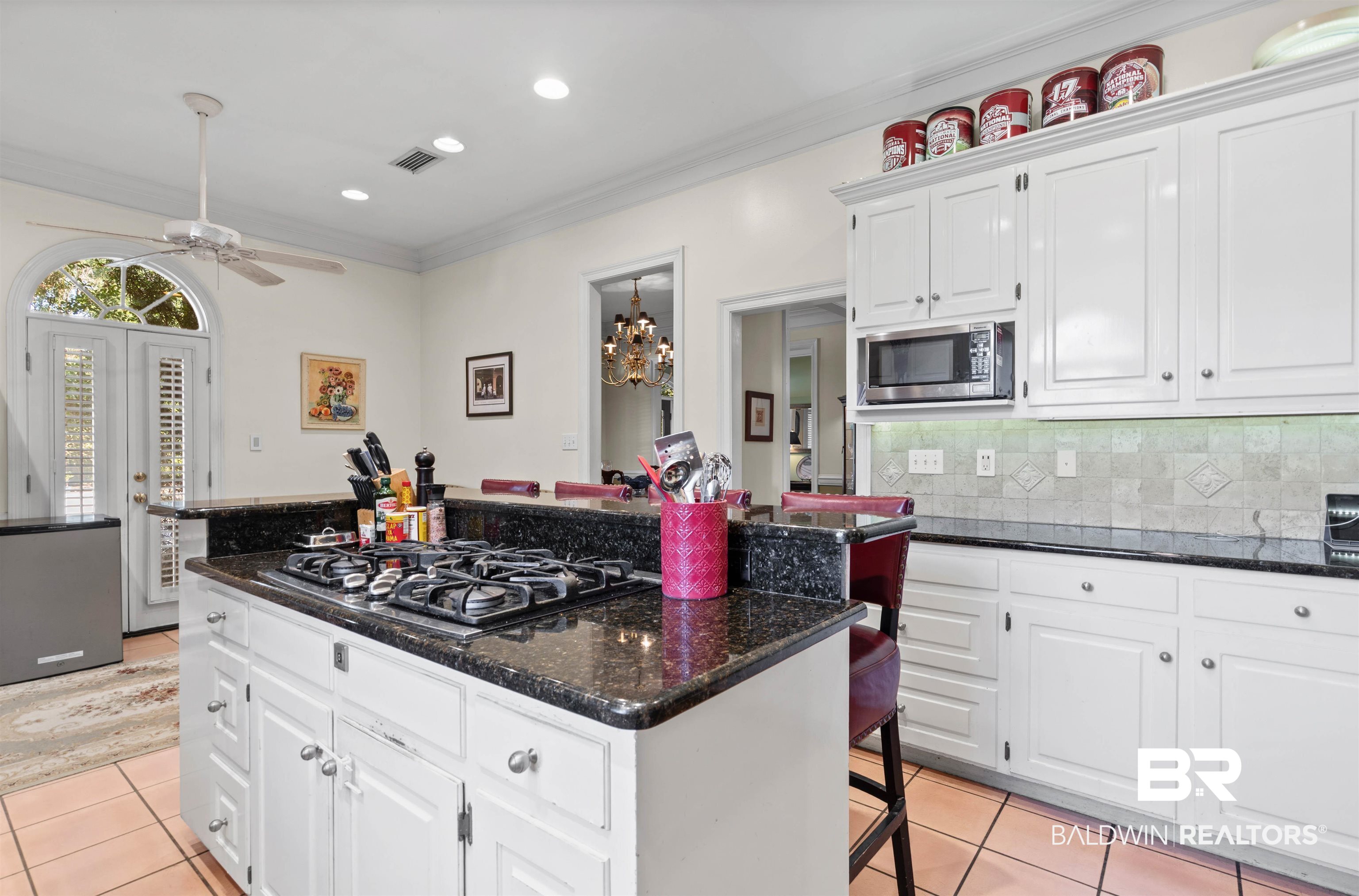 107 Beaver Dam Road Fairhope, AL 36532 - Photo 5 of 45 Kitchen featuring dark stone countertops, white cabinetry, a breakfast bar area, ornamental molding, and light tile patterned floors