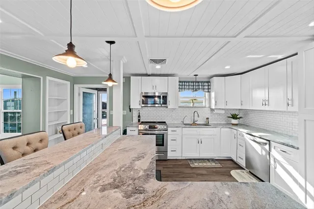 a large white kitchen with stainless steel appliances granite countertop a stove a sink dishwasher a dining table and chairs with wooden floor