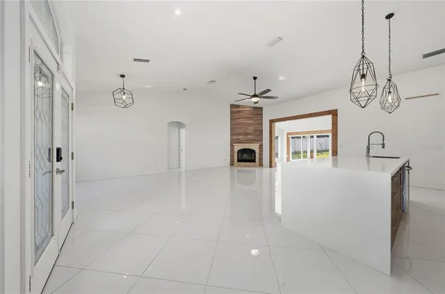 a view of an empty room with chandelier fan and kitchen view