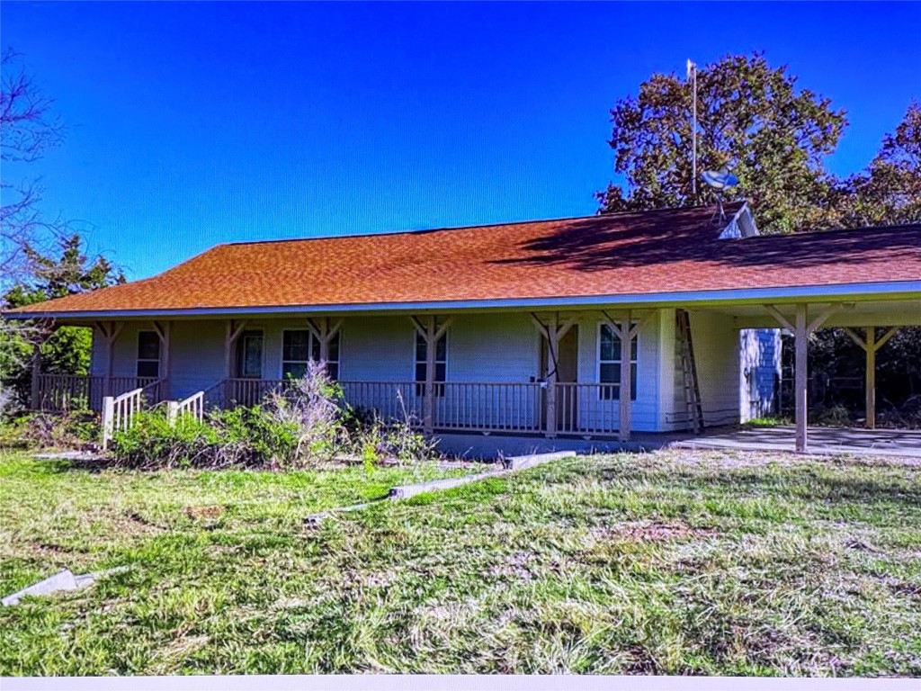 Farmhouse featuring covered porch, roof with shingles, an attached carport, and a front lawn