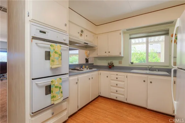 a kitchen with stainless steel appliances granite countertop a refrigerator a sink dishwasher a stove and white countertops with wooden floor