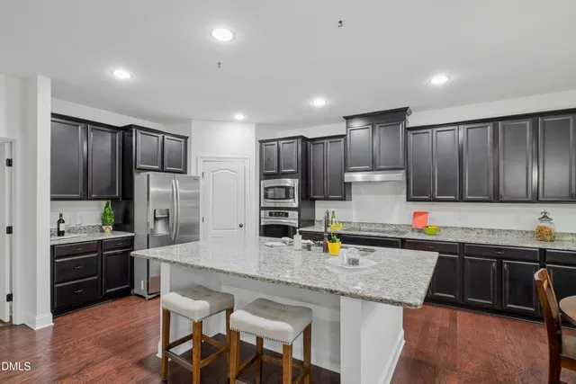 a kitchen with granite countertop a refrigerator a stove a sink a dining table and chairs