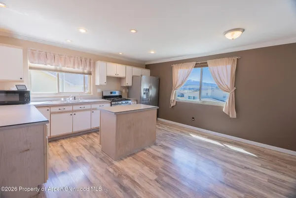 a large kitchen with stainless steel appliances granite countertop a stove top oven a sink dishwasher and white cabinets with wooden floor