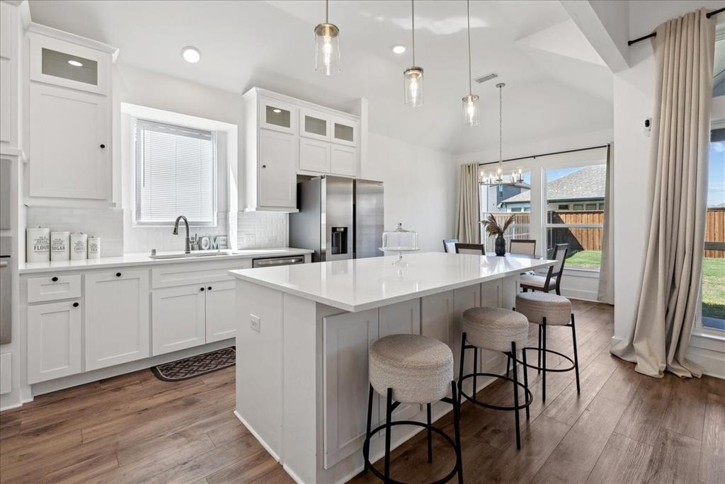 1710 Highwood Road Forney, TX 75126 - Photo 17 of 25 Kitchen featuring a large central island with seating, white cabinetry, integrated stainless steel appliances, wood-finish flooring, and a dining area with backyard access