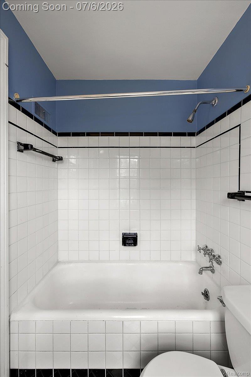 1051 Devonshire Road Grosse Pointe, MI 48230 - Photo 50 of 98 Bathtub and shower combination featuring white square tiling, a black accent tile border, and a chrome shower rod