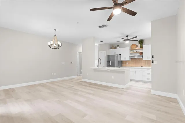 an empty room with kitchen view and a ceiling fan