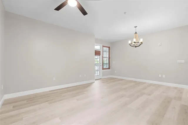 an empty room with chandelier fan and windows