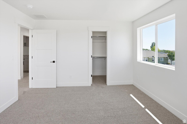 1315 West 3200 South, Unit 17 Perry, UT 84302 - Photo 46 of 58 Carpeted room with white walls, a large window, a three-panel interior door with black hardware, and an open closet featuring shelving and a hanging rod
