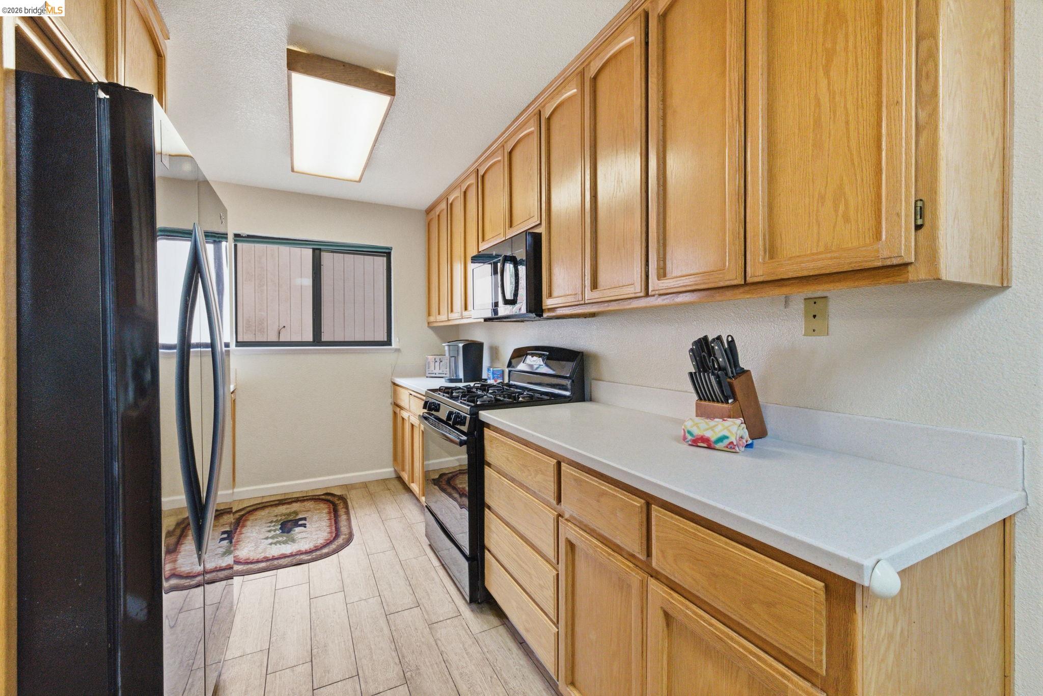 12068 Breckenridge Road Groveland, CA 95321 - Photo 20 of 55 Kitchen with black appliances, light countertops, wood tiled floors, a textured ceiling, and light wood finish cabinets