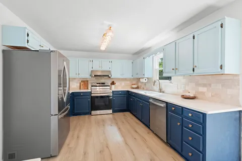 a kitchen with stainless steel appliances granite countertop a refrigerator a sink dishwasher a stove and white countertops with wooden floor