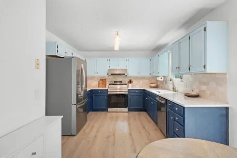 a kitchen with stainless steel appliances granite countertop a refrigerator a sink dishwasher a stove and white countertops with wooden floor