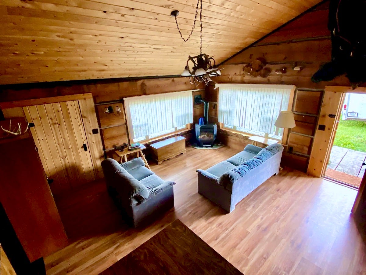 36 South Shore Road Babb, MT 59411 - Photo 4 of 21 Living room featuring a vaulted wood ceiling, a wood stove, wood finished floors, suspended lighting, and wooden walls