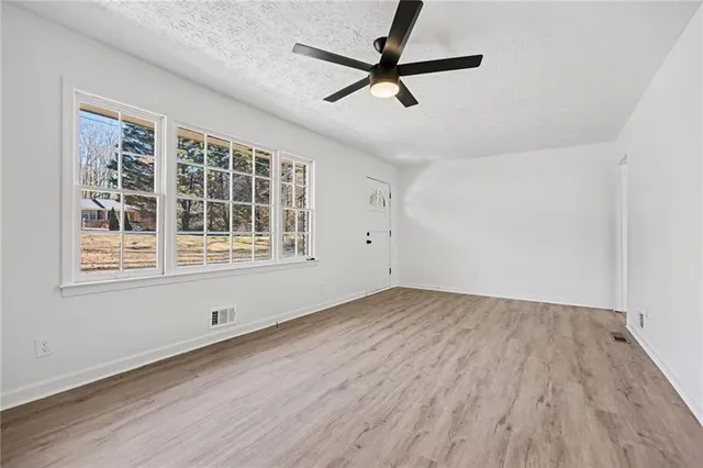 an empty room with wooden floor fan and windows