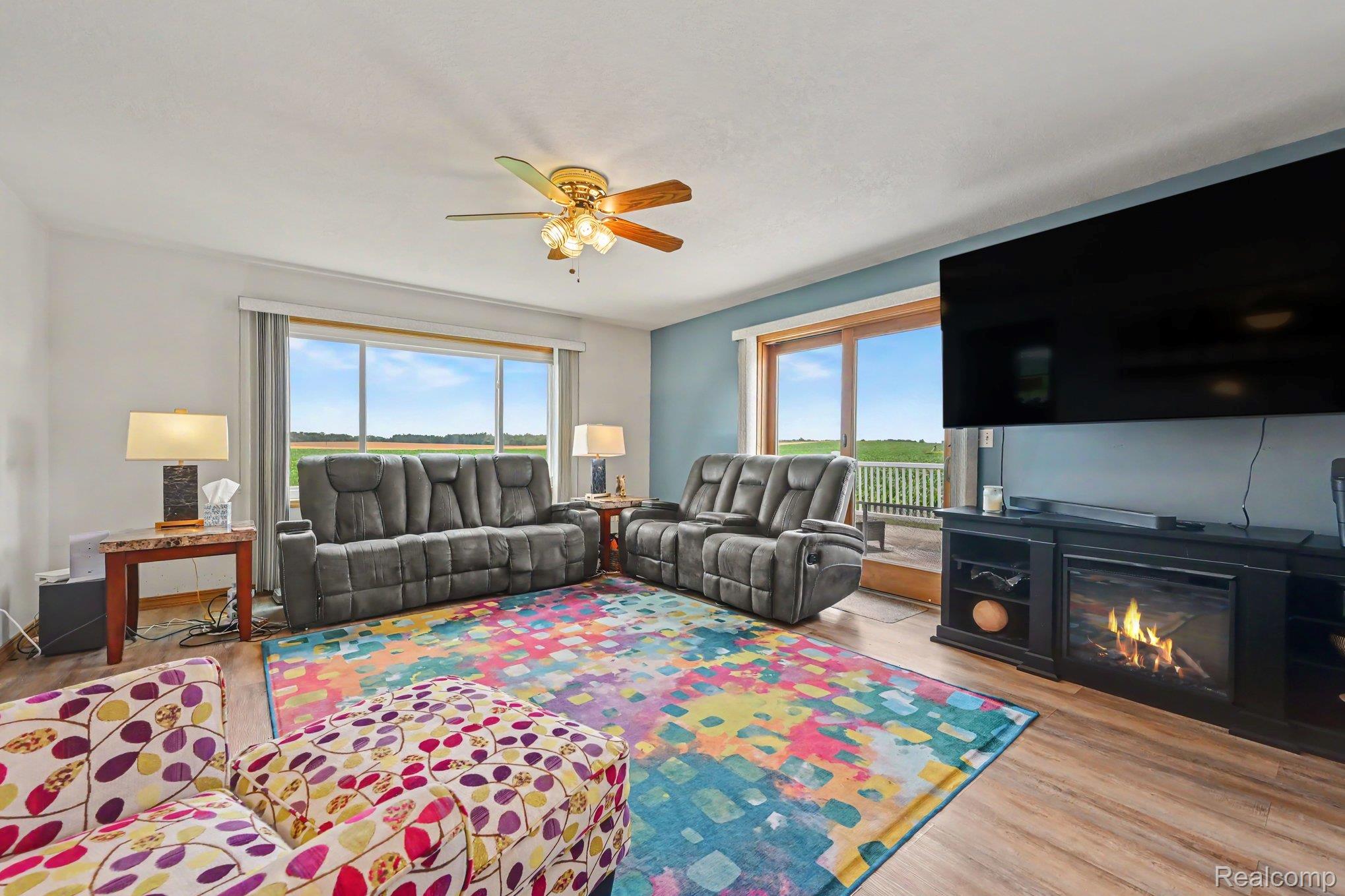 996 Arbogast Road Union City, MI 49094 - Photo 6 of 34 Spacious living area featuring expansive windows, wood-finish flooring, a ceiling fan with integrated lighting, a built-in entertainment center with an electric fireplace, and a light blue accent wall