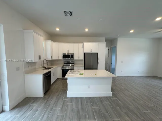 a large white kitchen with wooden floor and stainless steel appliances
