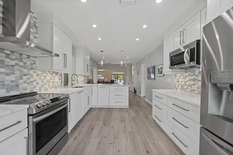a large kitchen with stainless steel appliances kitchen island granite countertop a stove a sink dishwasher and a oven with white cabinets
