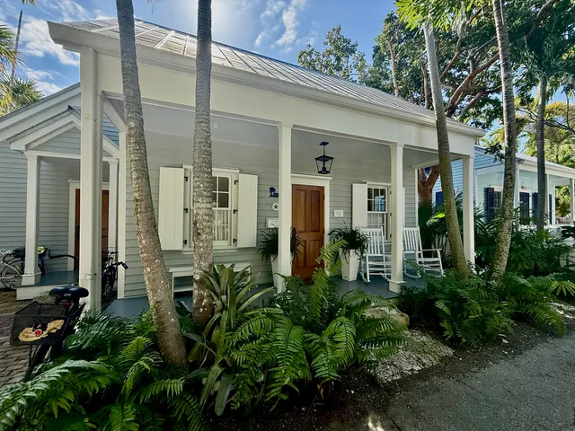 a view of a white house next to a yard with potted plants