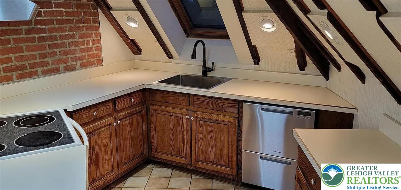 444 West 3rd Street, Unit 9 Bethlehem, PA 18015 - Photo 3 of 16 A compact kitchen with sloped ceilings features a skylight, rustic exposed beams, and a blend of brick and textured wall finishes.