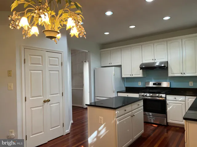 a kitchen with stainless steel appliances granite countertop a refrigerator a sink dishwasher a stove and a dining table with wooden floor