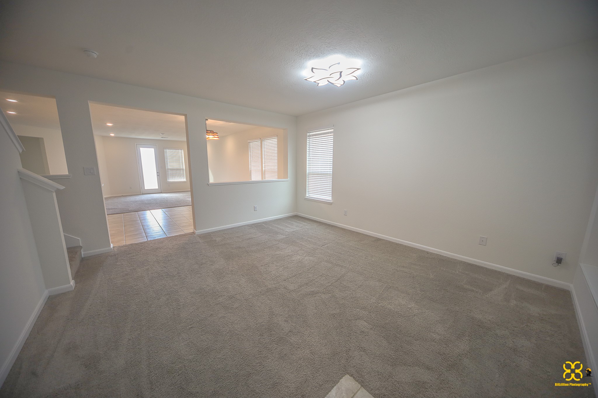 5820 Bluebonnet Lane Rosenberg, TX 77469 - Photo 11 of 43 This spacious living area features neutral carpeting, ample natural light from a large window, and a modern ceiling light fixture. It opens to a tiled area, offering a versatile layout for various furniture arrangements.