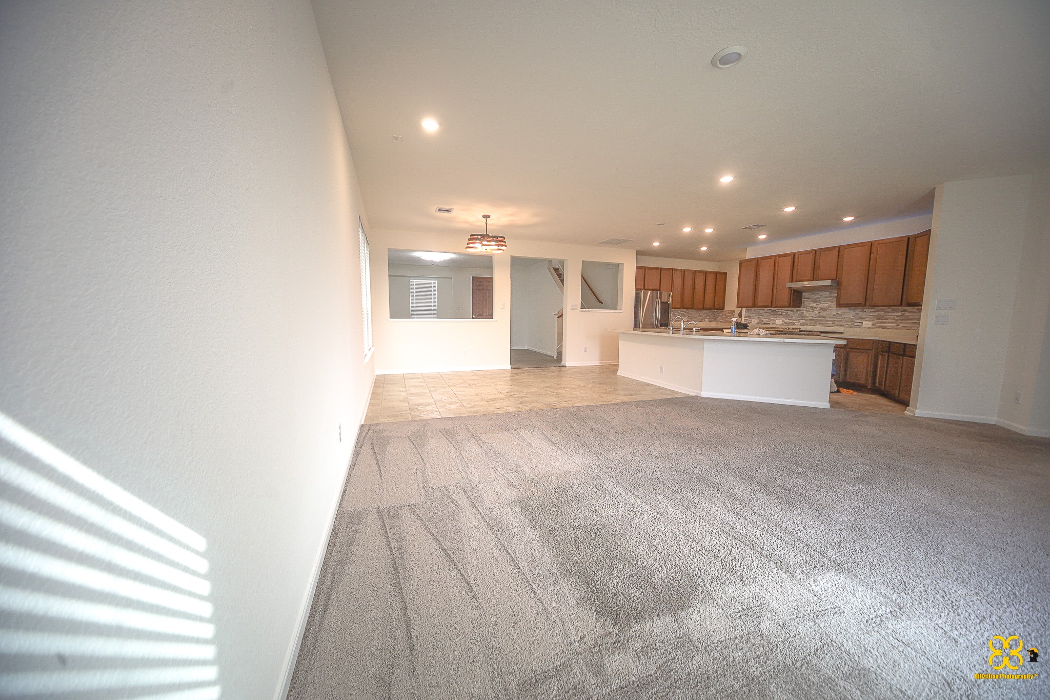 5820 Bluebonnet Lane Rosenberg, TX 77469 - Photo 18 of 43 Spacious open-concept living area with carpeted flooring and ample natural light. The kitchen features wooden cabinetry, a large island, and modern appliances, perfect for entertaining.