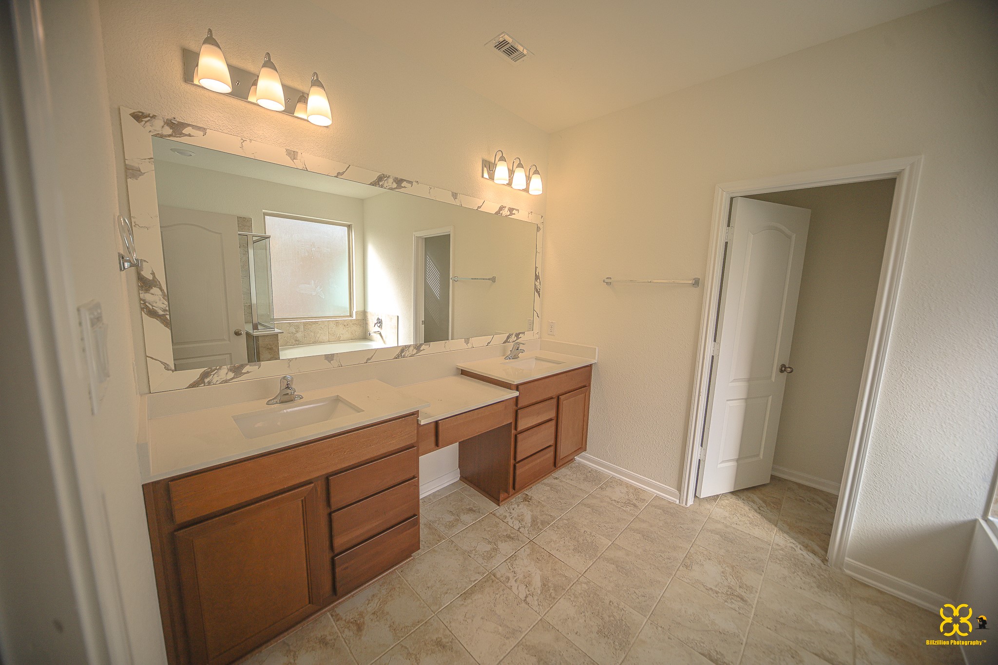 5820 Bluebonnet Lane Rosenberg, TX 77469 - Photo 25 of 43 Bright and spacious master Bathroom featuring a large marble-framed mirror, dual sinks with wooden cabinetry, and elegant tile flooring. Ample natural light from a frosted window enhances the clean, modern design.