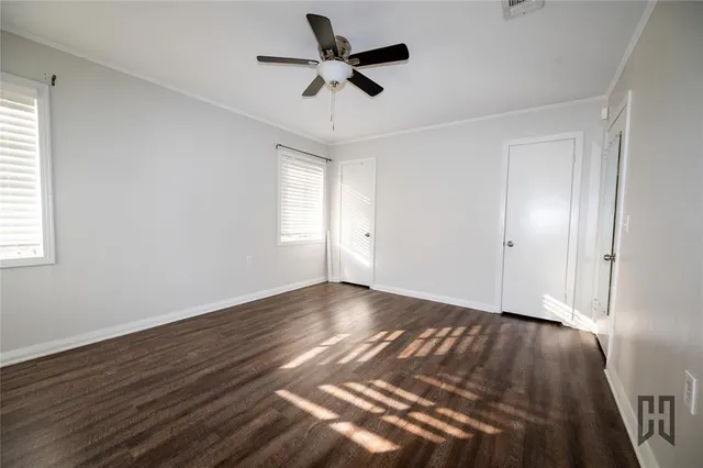 a view of an empty room with wooden floor and a ceiling fan