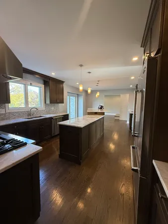 a kitchen with stainless steel appliances kitchen island granite countertop a refrigerator a sink dishwasher and a stove with wooden floor