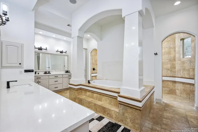 a large white bathroom with a tub a sink and a large mirror