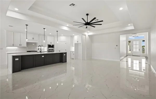 a large kitchen with stainless steel appliances kitchen island a large counter top a stove a refrigerator with white cabinets and wooden floor