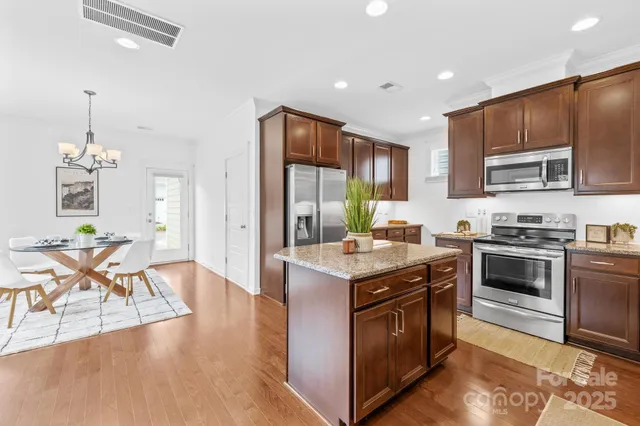 a kitchen with stainless steel appliances granite countertop a stove top oven a sink dishwasher a dining table and chairs with wooden floor