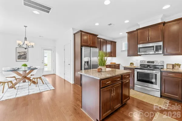 a kitchen with stainless steel appliances granite countertop a stove top oven a sink dishwasher a dining table and chairs with wooden floor