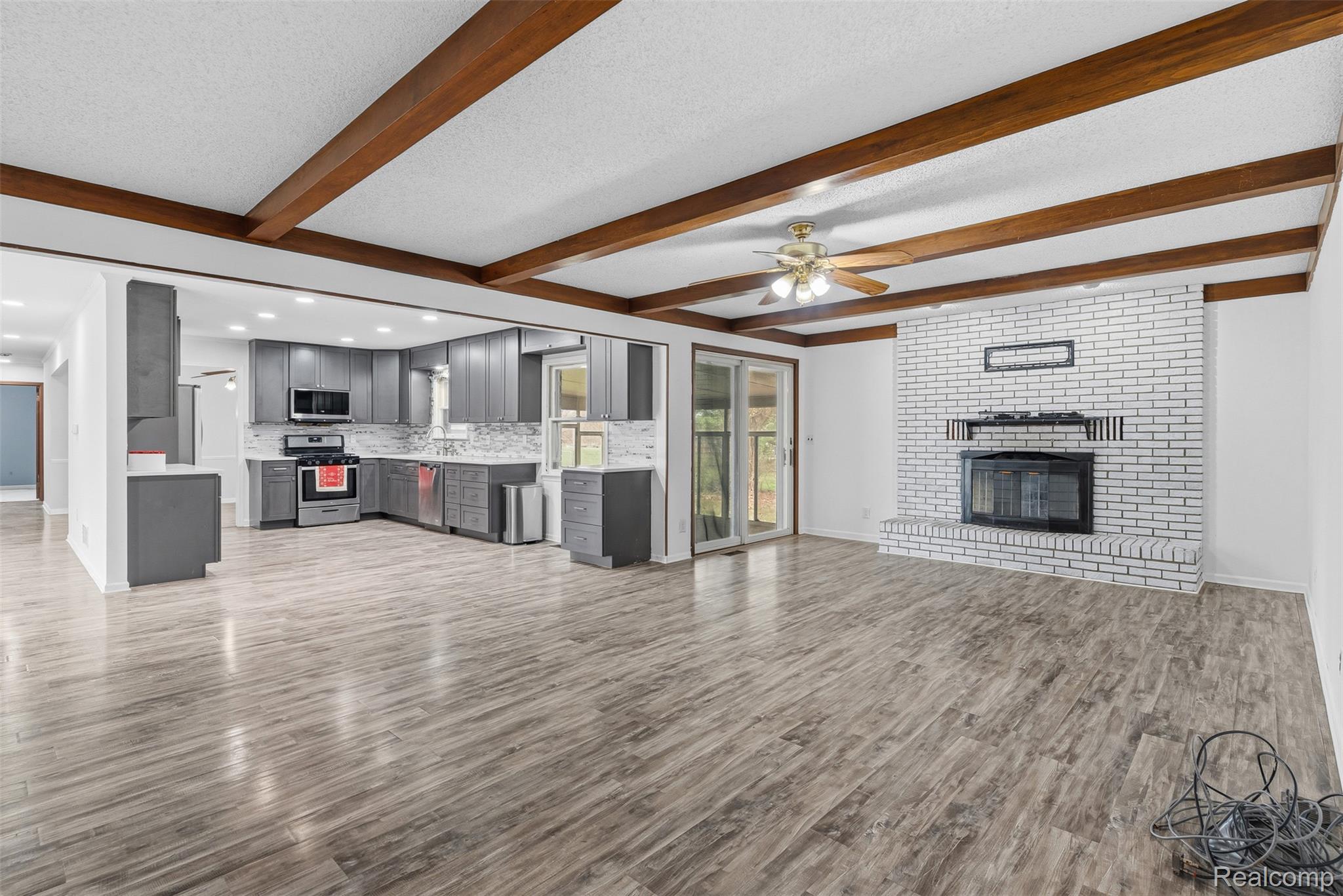 3432 South State Road Davison, MI 48423 - Photo 30 of 58 Unfurnished living room with a ceiling fan, dark wood-type flooring, a brick fireplace, a textured ceiling, and beam ceiling