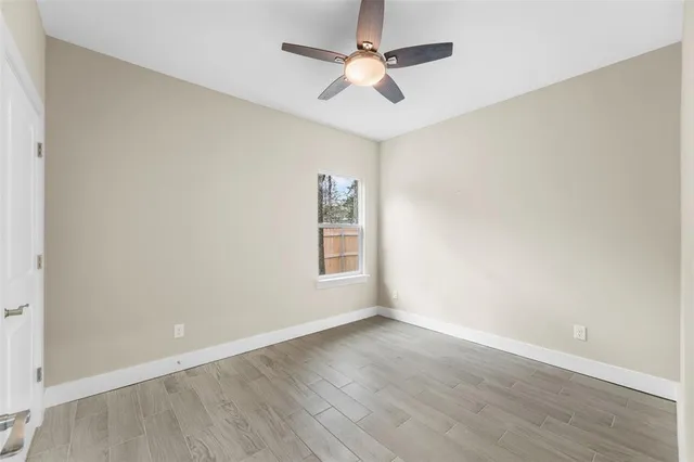 an empty room with wooden floor ceiling fan and windows