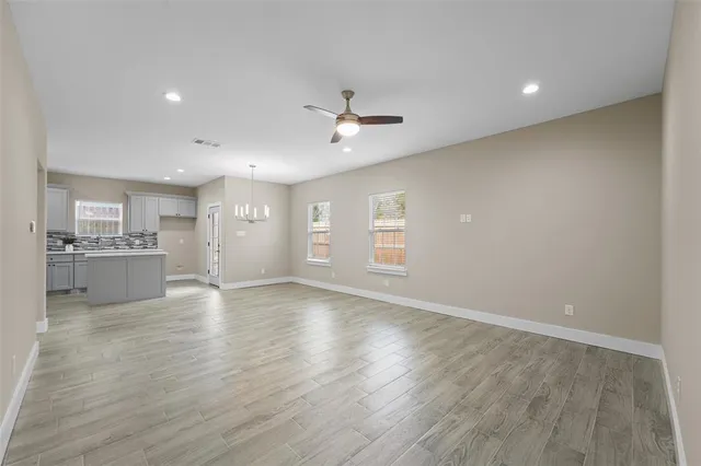 a view of an empty room and kitchen with wooden floor