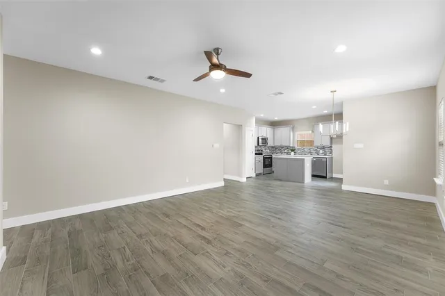 an empty room with wooden floor kitchen view and a window