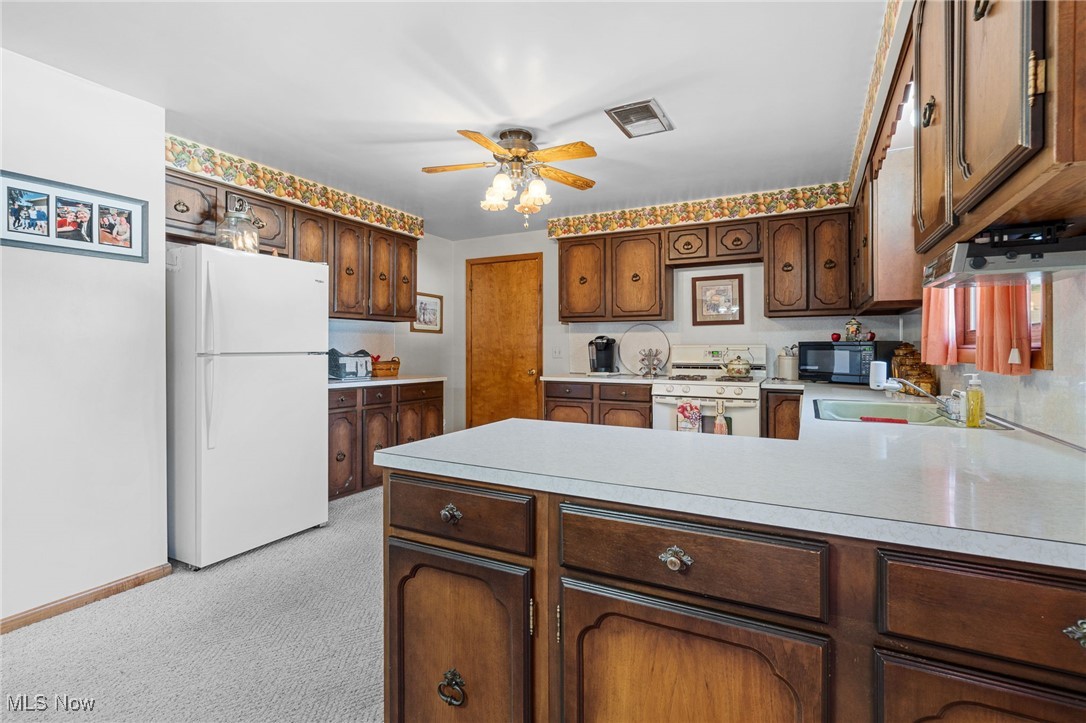 Kitchen with white appliances, light countertops, light colored carpet, a ceiling fan, and a peninsula