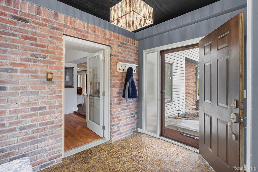 11111 Hibner Road Hartland, MI 48353 - Photo 11 of 59 Foyer entrance featuring brick wall, suspended lighting, and brick patterned floors
