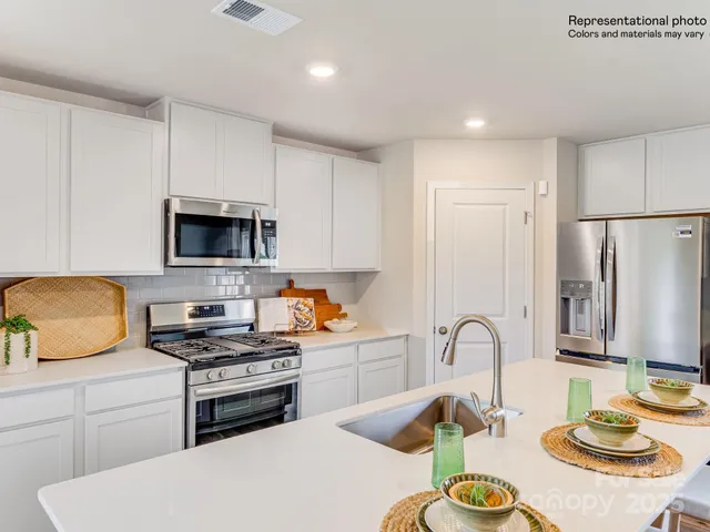 a kitchen with stainless steel appliances a dining table chairs refrigerator and microwave