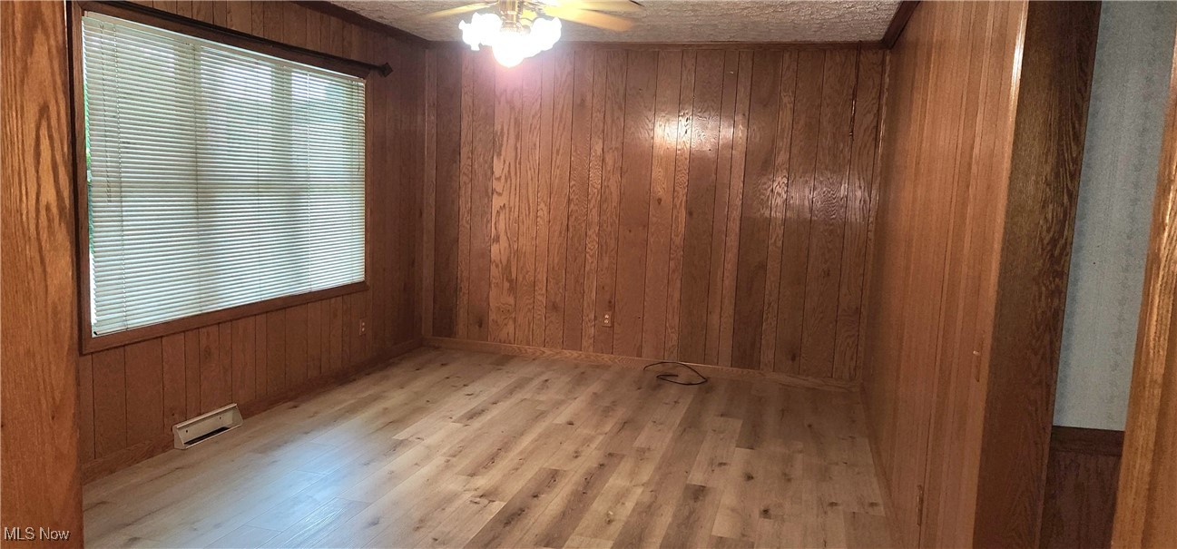 9090 Radcliffe Road Adamsville, OH 43802 - Photo 7 of 19 Spare room with a textured ceiling, ceiling fan, wood walls, and wood-type flooring