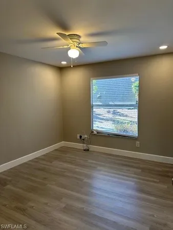 a view of an empty room with wooden floor and fan