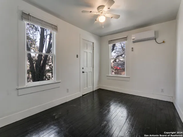 an empty room with wooden floor chandelier fan and windows