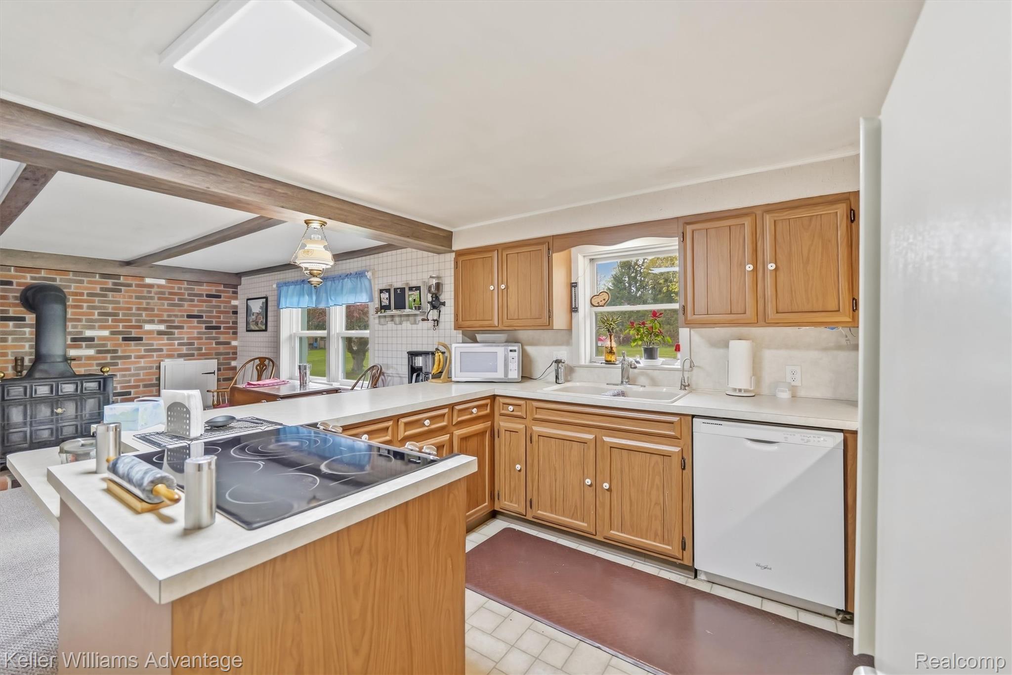 6595 Bray Road Vassar, MI 48768 - Photo 17 of 64 Kitchen featuring a peninsula, light countertops, white appliances, a wood stove, and beamed ceiling