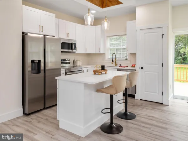 a kitchen with stainless steel appliances a refrigerator a sink a stove and white cabinets with wooden floor