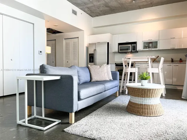 a living room with stainless steel appliances furniture a rug and a window