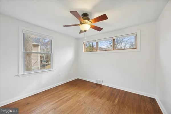 a view of an empty room with wooden floor and a ceiling fan