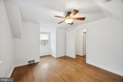 a view of an empty room with wooden floor and a ceiling fan