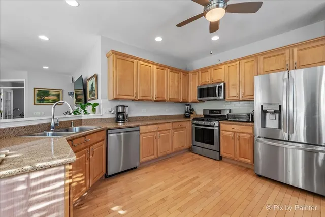 a kitchen with stainless steel appliances granite countertop a refrigerator a stove top oven a sink and dishwasher with wooden floor