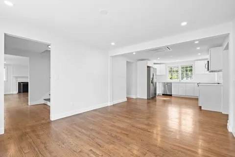 a view of an empty room with wooden floor and a kitchen
