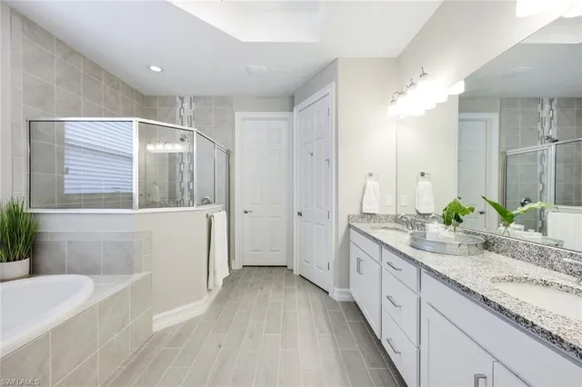 a spacious bathroom with a granite countertop double vanity sink a mirror and a bathtub